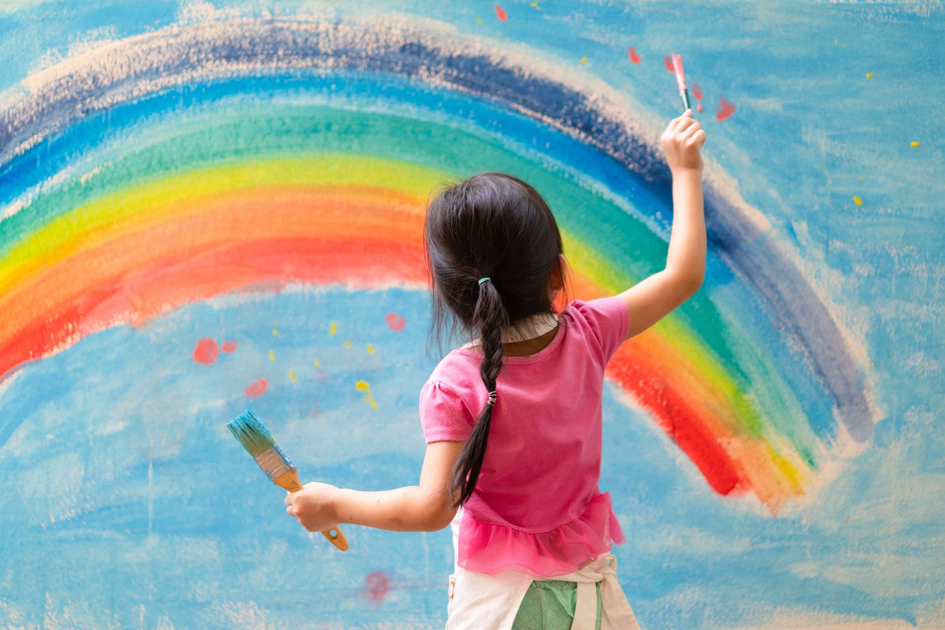 Girl painting rainbow and blue sky on large canvas