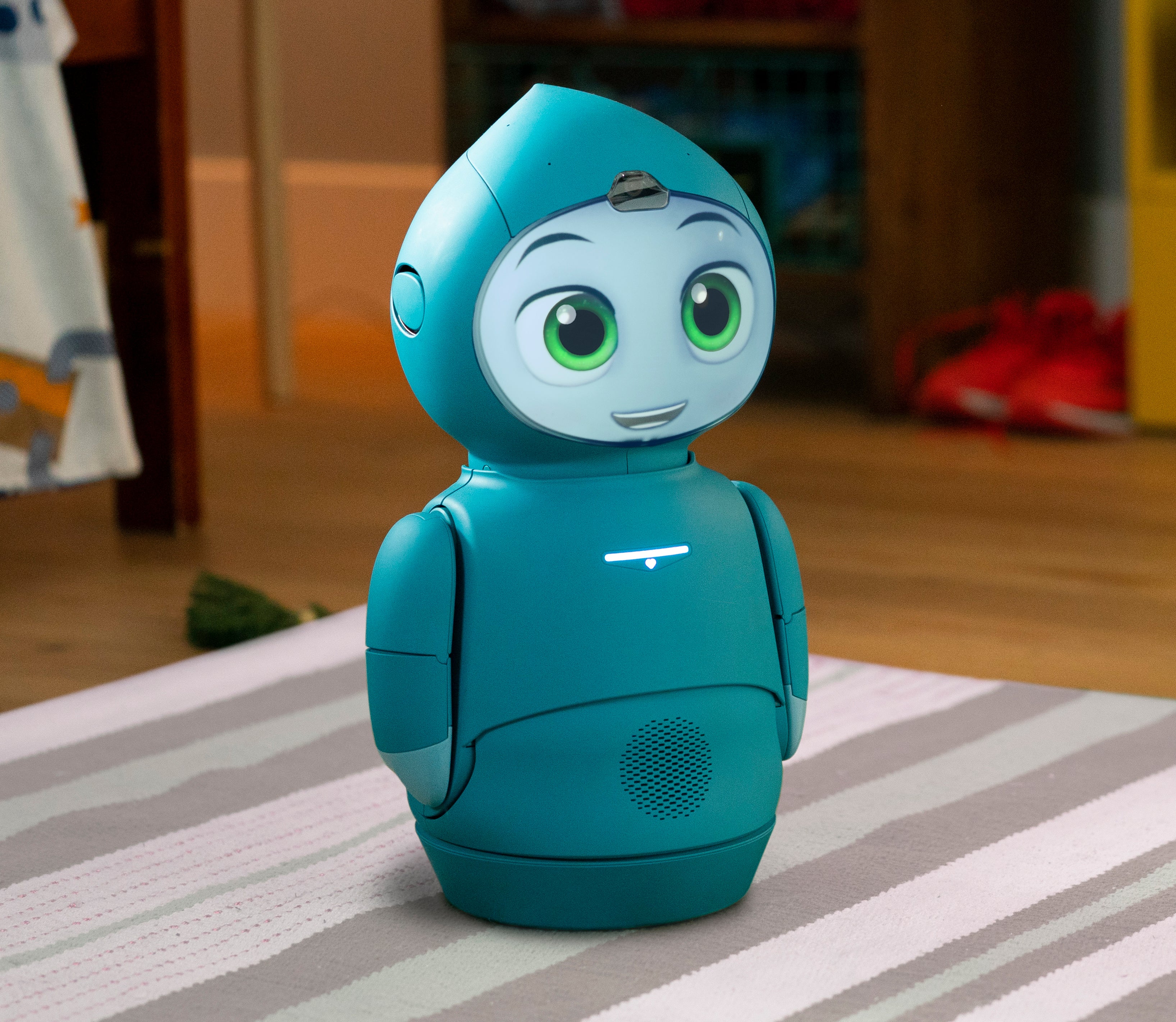Moxie Robot smiling, standing on grey carpet in their mentor home